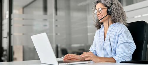 An image of someone with a headset, working at a laptop
