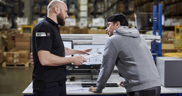 Image of two people in a warehouse infront of a computor